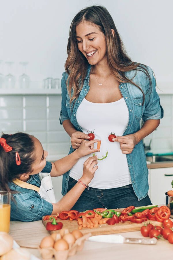 Pregnant mother and daughter making vegetable smiley face